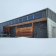 Bâtiment moderne avec panneaux solaires, portes en bois et neige.