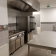 Cuisine professionnelle avec plaque de cuisson, four, hotte, réfrigérateur, plan de travail et évier.