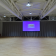 Salle vide avec écran, rideaux, projecteurs et parquet.