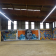 Atelier avec graffitis muraux, sol en béton, fenêtres et éclairage fluorescent.