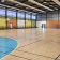Gymnase avec panneaux de basket, but de handball, parquet, gradins et portes de sortie.
