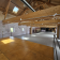Salle spacieuse avec poutres apparentes, sol en bois, murs en brique, rampes et fenêtres.