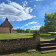 Petit bâtiment avec toit pointu, pelouse, ciel nuageux, arbres, mur de pierre, escaliers.