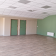 Salle vide avec portes vertes, radiateur et plafond à dalles.