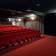 Salle de cinéma avec rangées de sièges rouges, écran et projecteur.