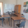 Salle de classe avec tables, chaises, tableau blanc, armoire et affiches.