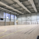 Salle de sport avec parquet, paniers de basket, gradins, panneaux de score et éclairage au plafond.