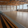 Gymnase avec parquet, gradins, panier de basket et fenêtres.
