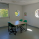 Salle avec table, chaises, fenêtres rondes et rectangulaire, affiches.