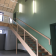 Escalier en bois avec rampe, mur vert, éclairage mural, plafond en panneaux.