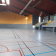 Salle polyvalente avec terrain de sport, gradins, murs métalliques et toit incliné.