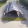 Hangar avec toit métallique, accès ouvert, aire de béton, graminées environnantes.