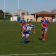 Match de rugby avec joueurs en action, portant des maillots rouges et bleus, sur un terrain herbeux.