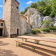 Ancienne église en pierre avec bancs et tables en bois à l'extérieur, rochers et végétation.