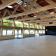 Salle spacieuse avec chaises, grandes fenêtres et structure en bois.