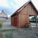 Bâtiment en bois avec porte rouge, vélo jaune, maison en arrière-plan.
