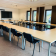 Salle de réunion avec tables en U, chaises, écran et fenêtres.