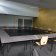 Salle avec tables disposées en U, chaises, murs gris et jaune, portes, et éclairage au plafond.