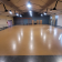 Salle spacieuse avec éclairage suspendu, sol en bois, mezzanine, portes et fenêtres.