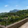 Chemin de pierre avec garde-corps métallique, vue sur village et montagnes.