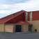Bâtiment industriel avec toit rouge, murs beiges et bruns, porte de garage et entrée principale.