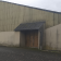Bâtiment industriel avec murs en béton et tôle, toiture en pente, deux portes de garage et une petite entrée.