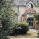 Maison avec toit en ardoise, briques apparentes, porte d'entrée et végétation environnante.