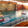 Salle de sport avec tapis, cheval d'arçons, barres parallèles, barre fixe, agrès, trampoline et gradins.