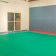 Salle avec sol vert, mur gris, porte grillagée, raquettes, et porte-manteau.
