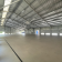 Grand espace vide avec toit métallique, murs en brique, sol en béton.