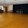Salle avec parquet, chaises, table, rideau noir, horloge, bureau et porte rouge.