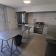 Cuisine avec table, poubelle, plaques de cuisson, évier, micro-ondes et étagères.