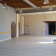 Salle vide avec porte, mur en pierre, porte-manteau, extincteurs et seuil de porte.