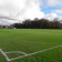 Terrain de football avec but, pelouse et ciel nuageux.