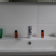 Lavabo avec robinet, deux flacons orange, vase vert et pot avec plante.
