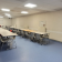 Salle de classe avec tables, chaises, tableau blanc et radiateurs.