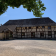 Maison à colombages, toit en chaume, entrée, fenêtres, arbre, ciel.