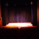 Salle de spectacle avec scène, rideaux, projecteurs, écrans latéraux et sièges.