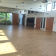 Salle spacieuse avec parquet, portes en bois, fenêtres, luminaires suspendus, et mobilier de jardin visible à travers les portes vitrées.