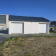 Bâtiment avec deux portes de garage blanches, toit plat, rampes d'accès et terrain herbeux.