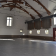 Grande salle avec plafond voûté en bois, murs blancs, fenêtres, porte, et sol en carreaux.