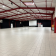 Salle spacieuse avec sol carrelé, piliers rouges, écran blanc, tableau d'affichage et distributeur automatique.