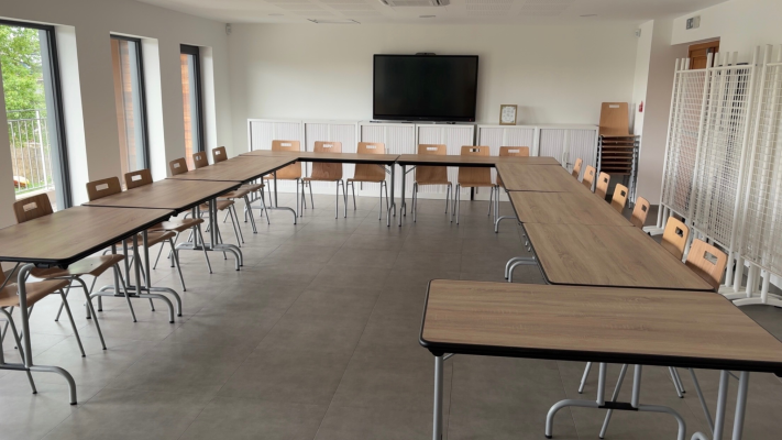 Salle de classe avec tables, chaises, écran et porte-manteau.