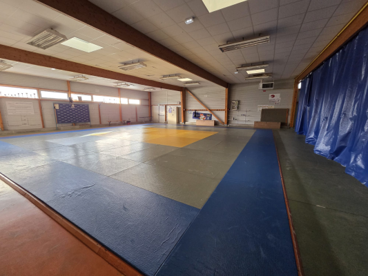 Salle de gym avec tatamis, tableau et rideau.