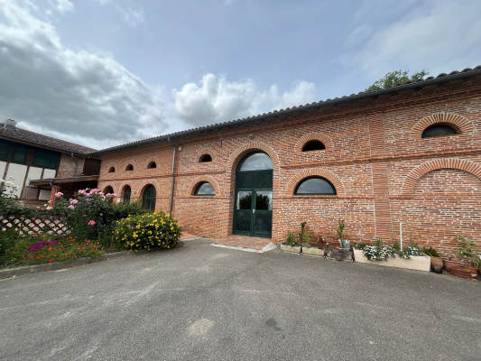 Bâtiment en brique avec arches, fleurs et parking.