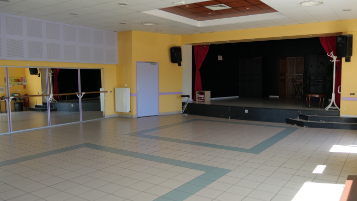 Salle avec barre de danse, scène, rideau, porte et miroir.