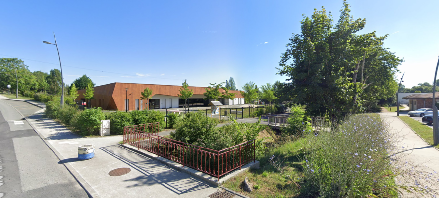 Bâtiment avec toits plats, arbres, buissons, clôture et route.