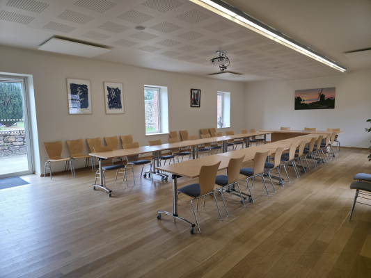 Salle de réunion avec tables, chaises et tableau blanc.