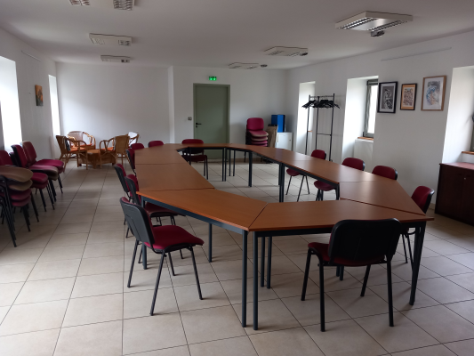 Salle de réunion avec tables, chaises, armoire, porte et sortie de secours.