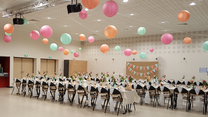 Salle avec tables, chaises, lanternes suspendues, fleurs et bannières.